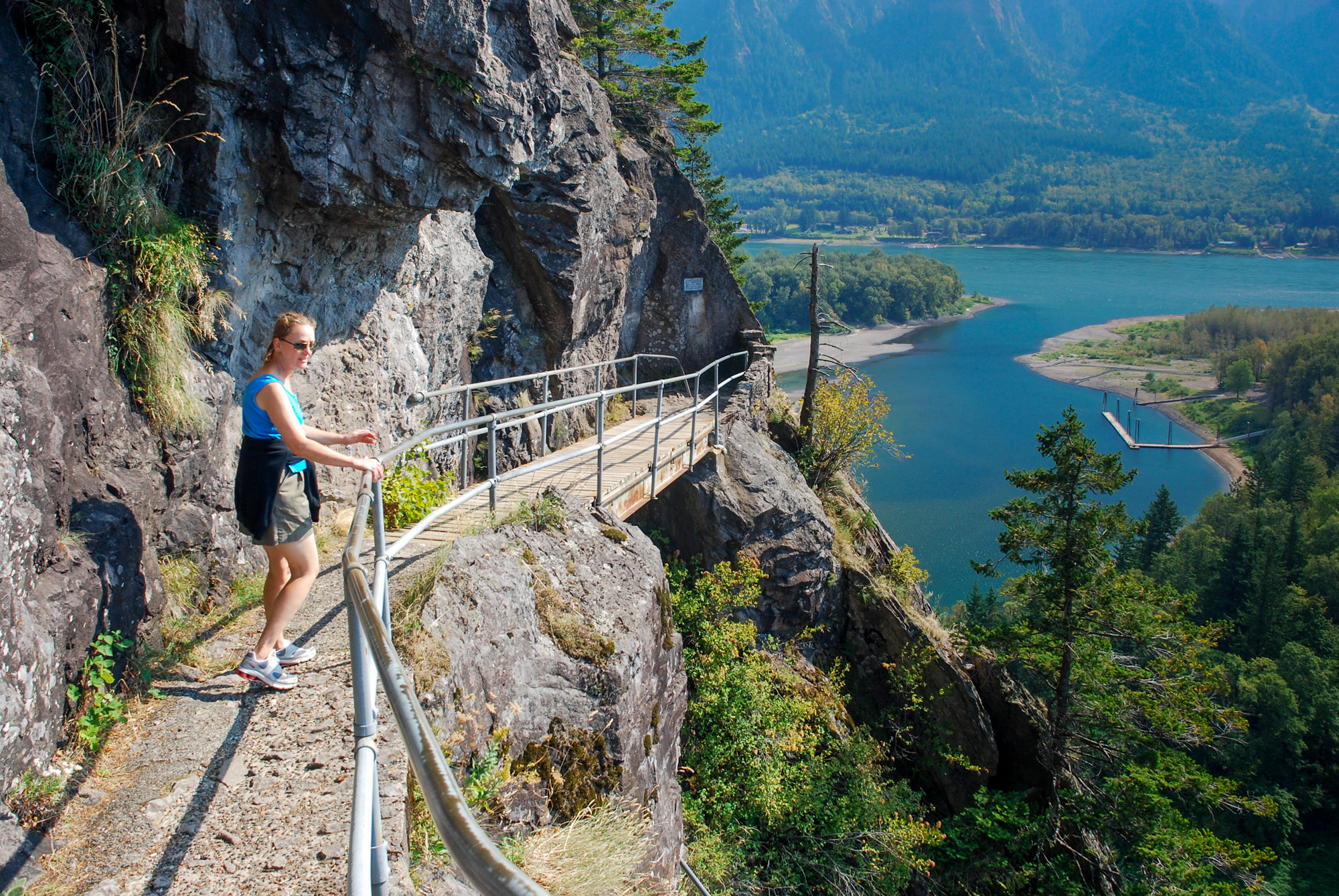 A hiker on a narrow railed walkway carved into Beacon Rock above the Columbia River